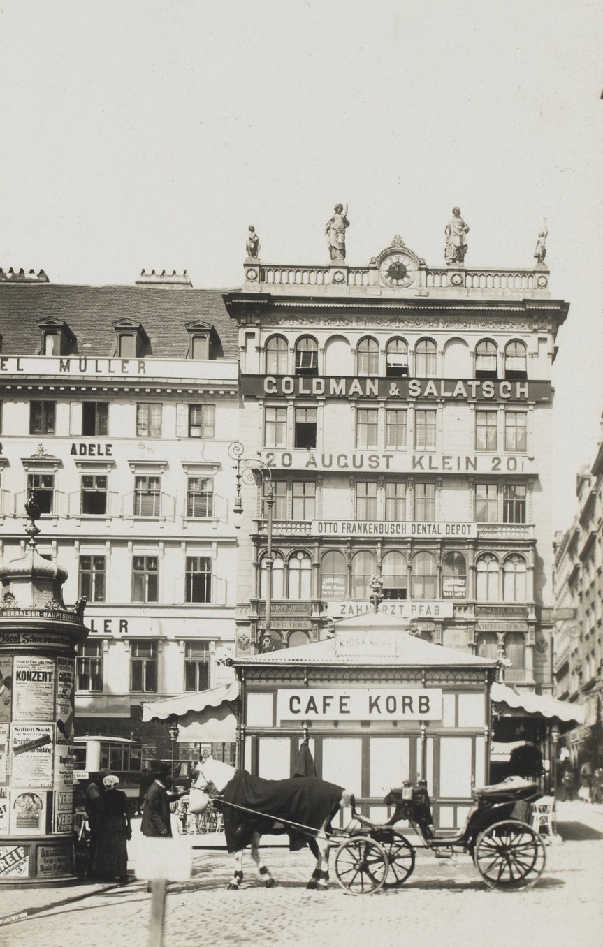 eine Fassadenansicht mit Gebäuden, vor den höheren Gebäuden ist, wesentlich niedriger, das Cafe Korb. Davor steht eine Kutsche.