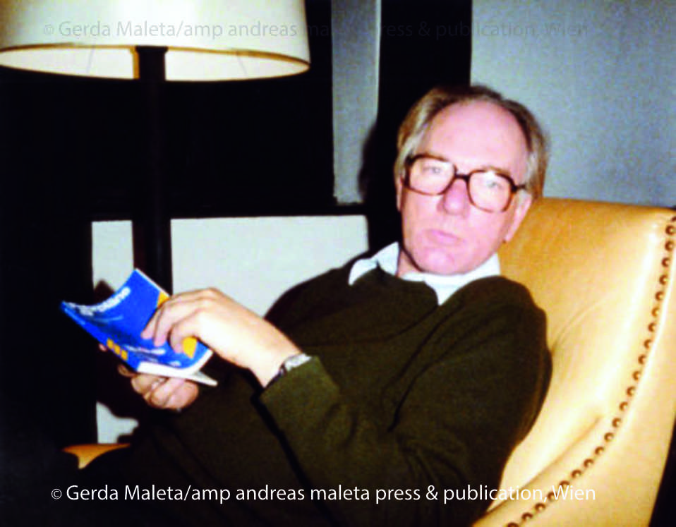(c) Gerda Maleta/amp andreas maleta press & publication, Wien Thomas Bernhard sitzt in einem gelben Ledersessel mit goldenen Knöpfen entlang der Lehne. Er schaut in die Kamera. In der Hand hält er ein Taschenbuch mit blauem Cover.