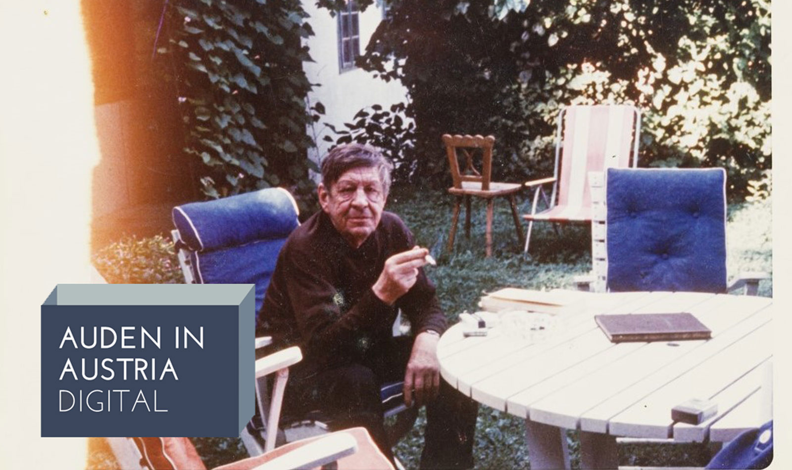 Wystan Hugh Auden sitting in a garden chair, smoking. The project logo is in the bottom left corner.