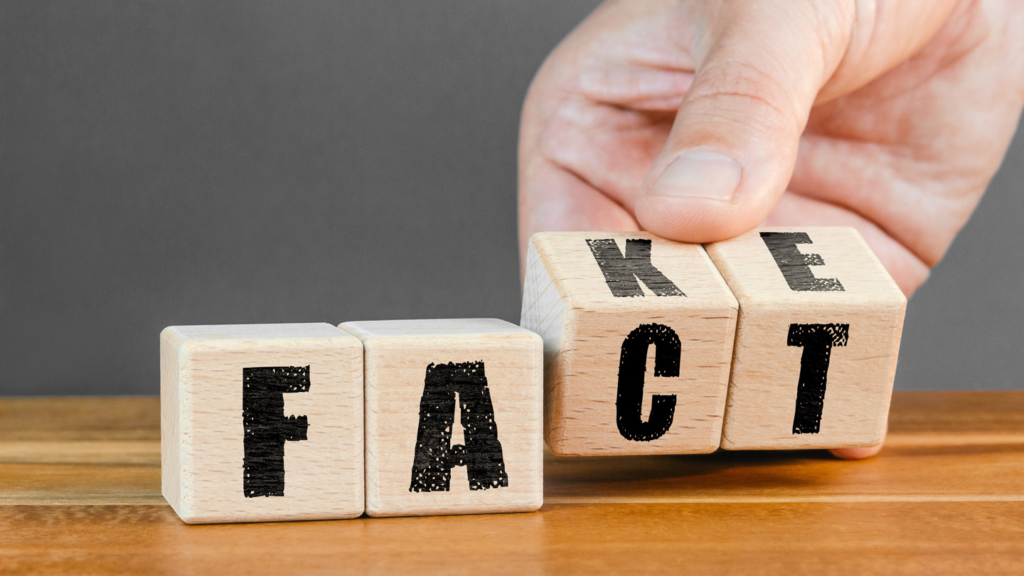 Würfel zeigen die Buchstaben F und A, dahinter dreht eine Hand zwei weitere Würfel von C T und K und E, um das Wort Fact zum Wort Fake zu ändern.