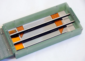Auf der Rückseite sind der Silizium-Sensor (grau), die Rippen (schwarz-weiß) und die um den Rand gefalteten Flex-Leiterplatten (orange) deutlich zu erkennen.