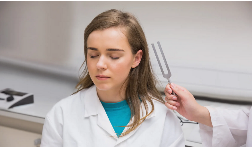 A woman with closed eyes undergoes a hearing test with a tuning fork.