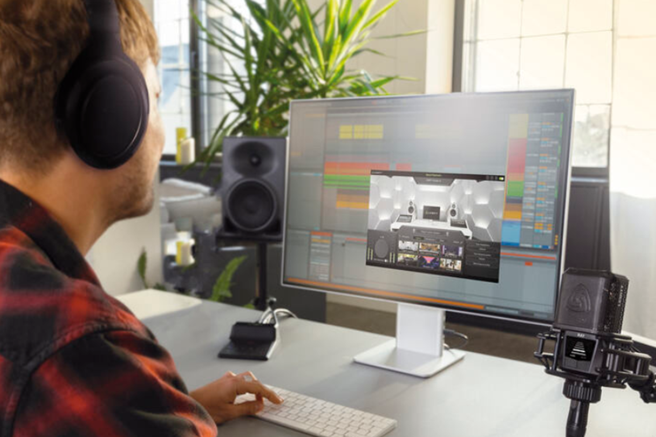 A person wearing headphones works at a computer audio setup, using software that displays a virtual studio environment on the monitor.