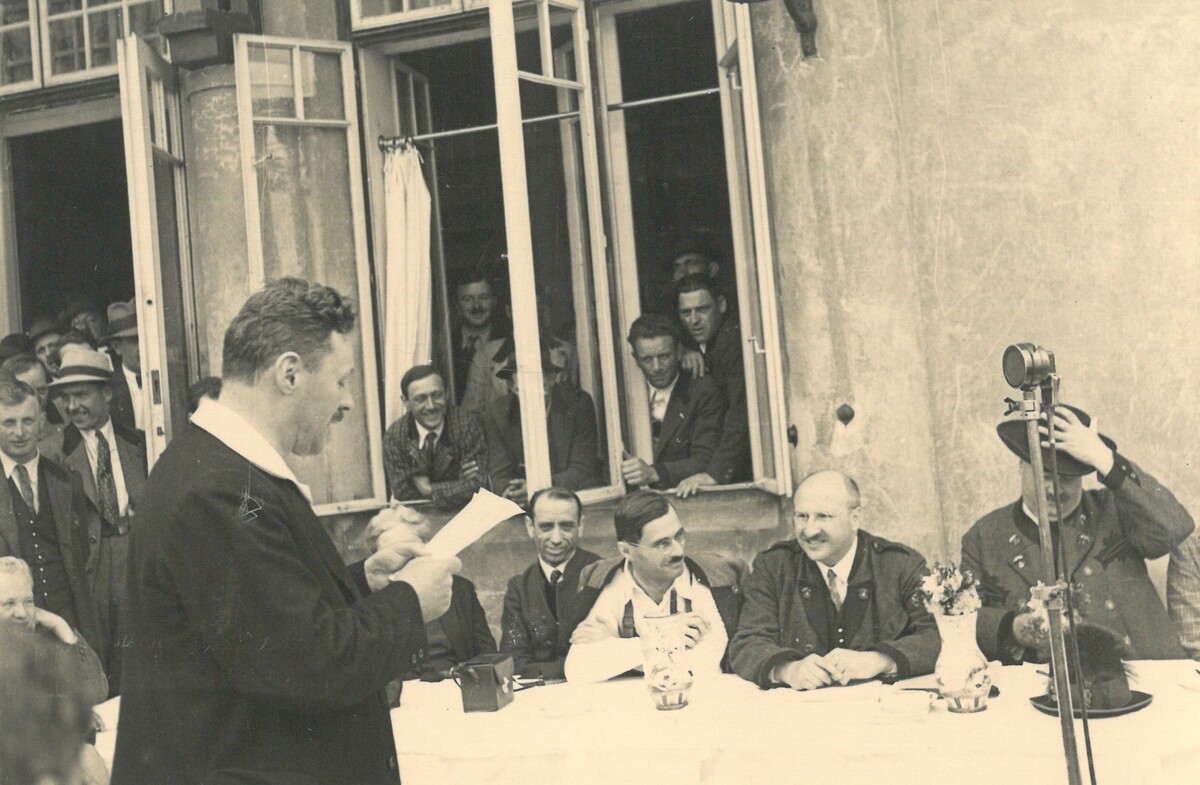 Teacher Karl Schauer (left, standing) and the jury (with Georg Kotek, 2nd from right, seated) at the Volksliedsingen der RAVAG in Payerbach, May 26th, 1935. © Archiv des Österreichischen Volksliedwerkes/ÖNB 