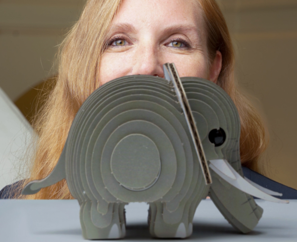 Biologist Angela Stöger behind a small gray cardboard elephant model.