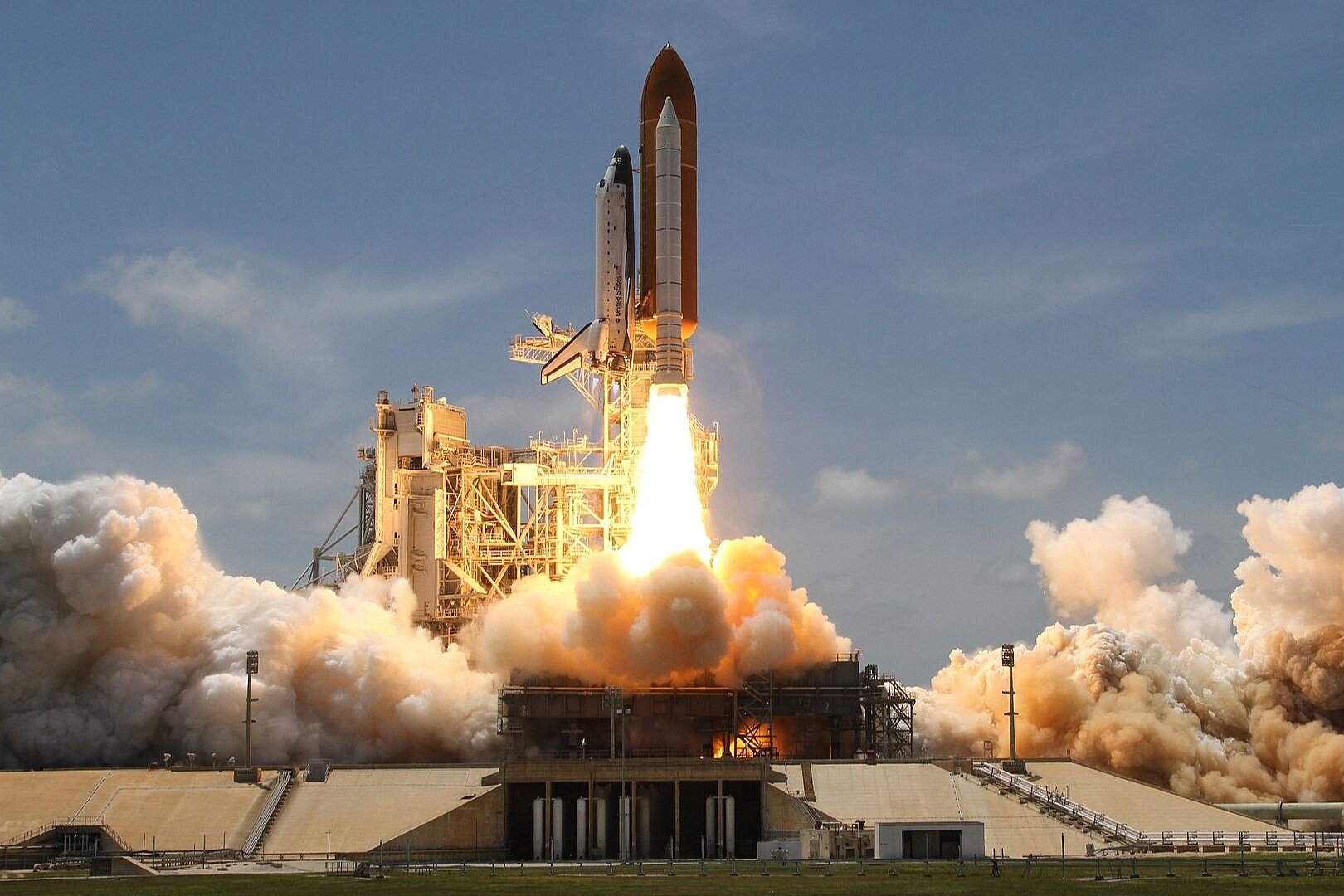 Start einer NASA-Raumfähre (Space Shuttle) von der Startrampe unter hellem Feuerschein und gewaltigen Rauchwolken.