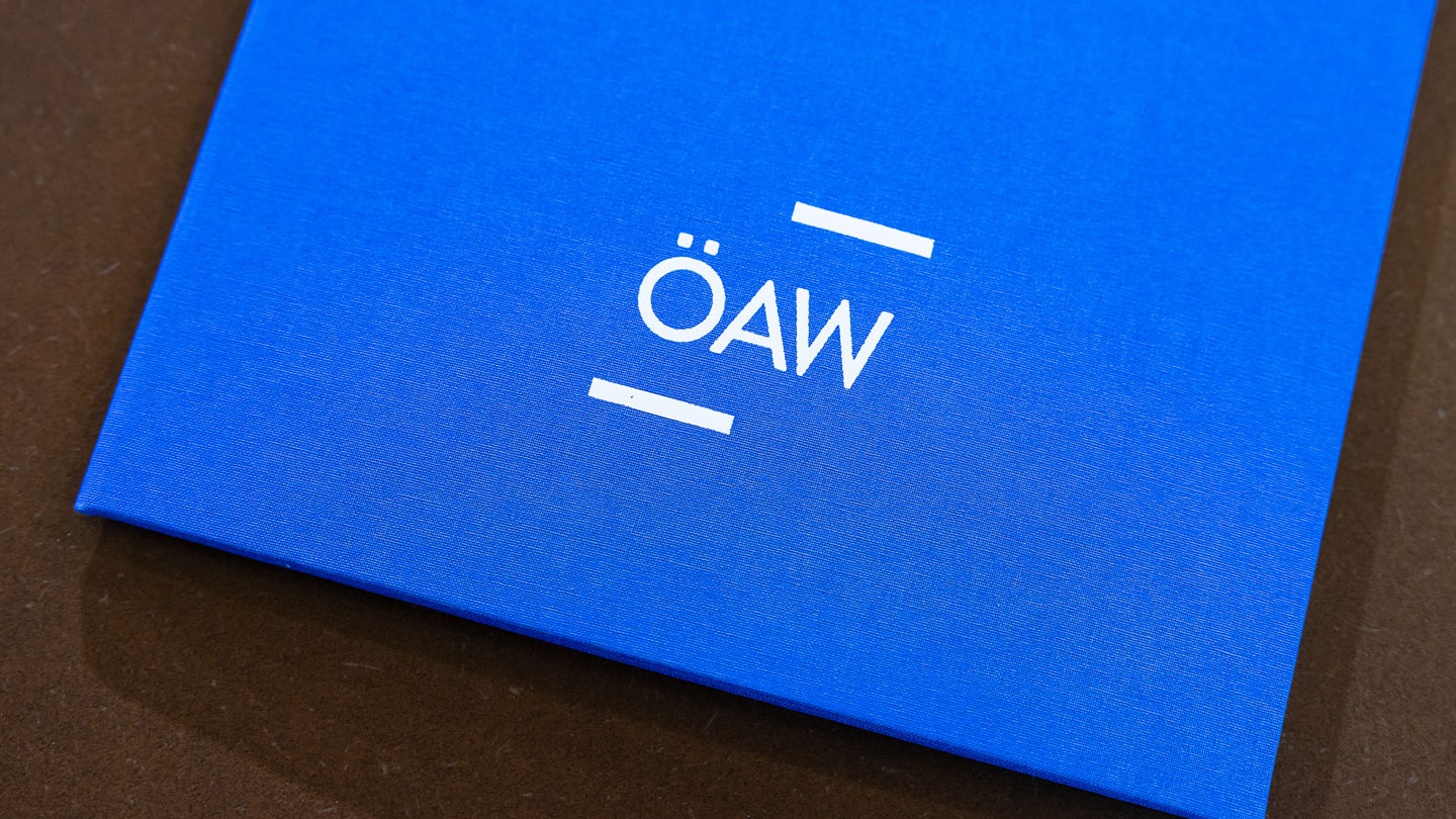 Foto einer Mappe mit ÖAW-Logo, in der die Stipendienurkunde überreicht wird.