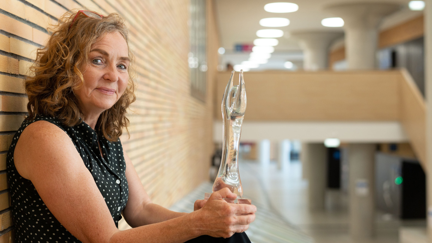 Wittgenstein-Preis an Christa Schleper Christa Schleper hält an einer Wand sitzend die gläserne Trophäe des Wittgenstein-Preises vor sich.