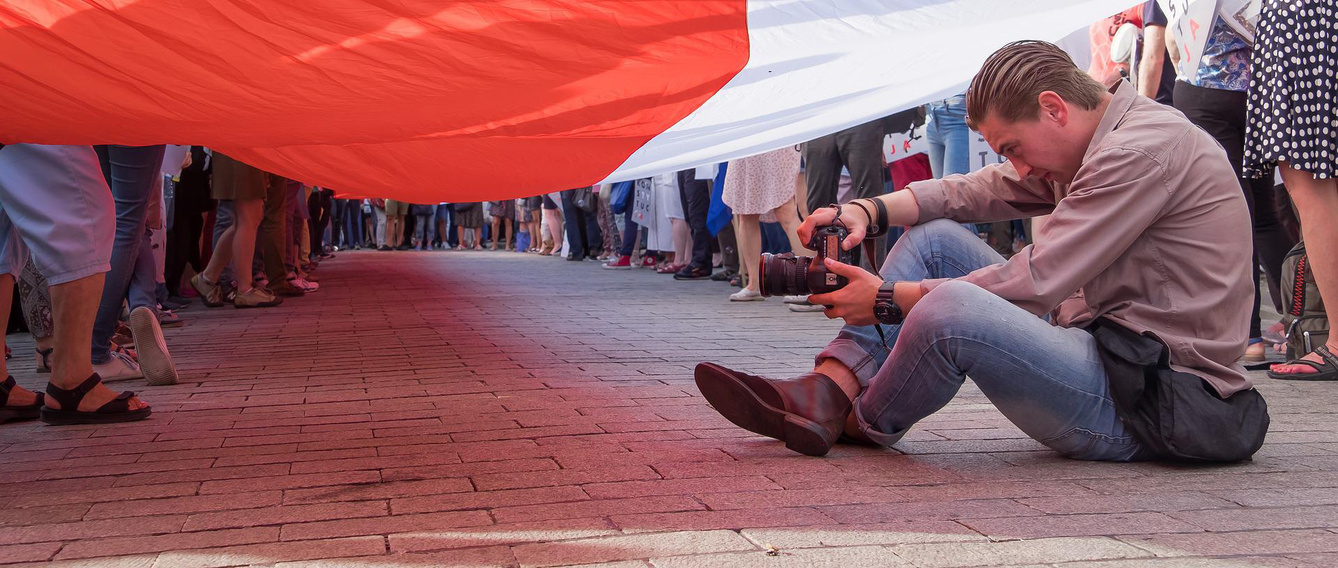 Medienfreiheit Ein Mann sitzt mit Kamera während einer Demonstration unter einer Flagge