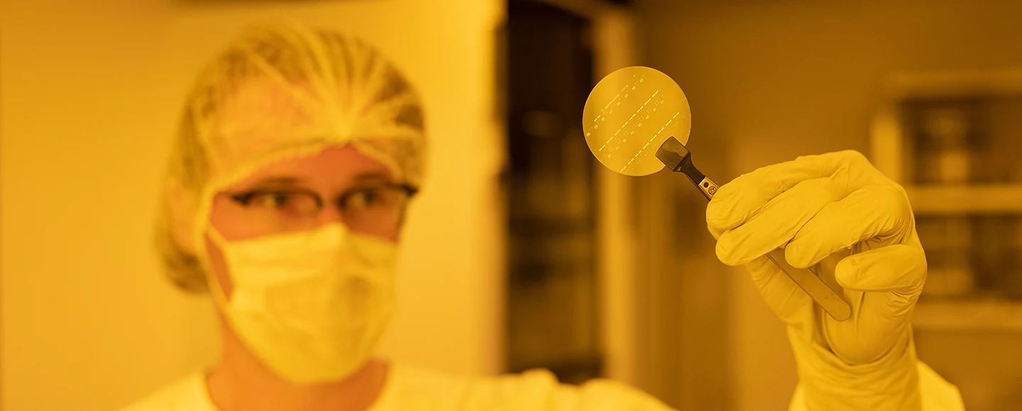 Ein Forscher blickt in einem Labor auf einen Halbleiter, den er in der Hand hält. 