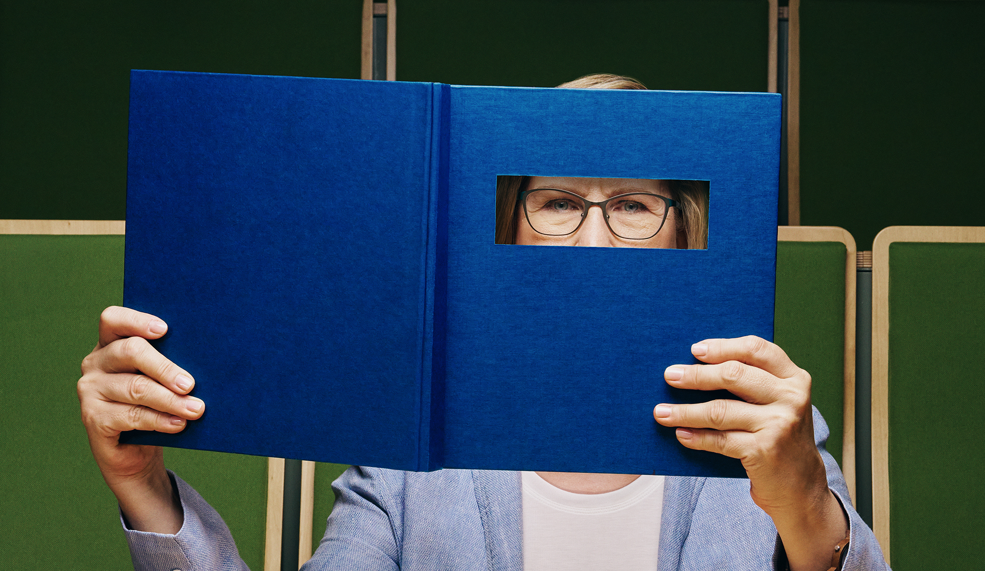 Eine Frau hält ein Buch mit einem Sehschlitz vor das Gesicht