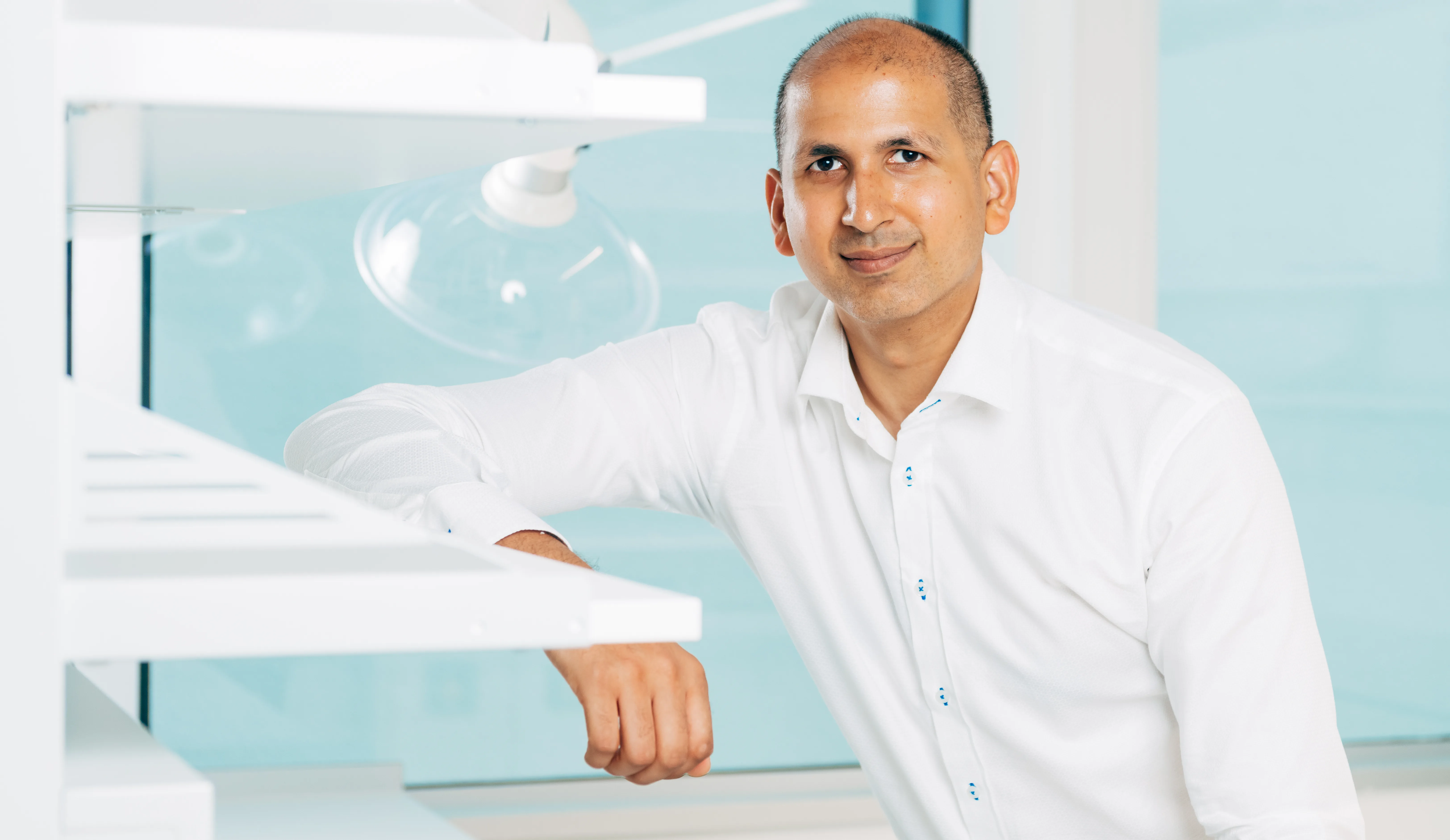 Wali Malik blickt angelehnt an ein Regal in die Kamera