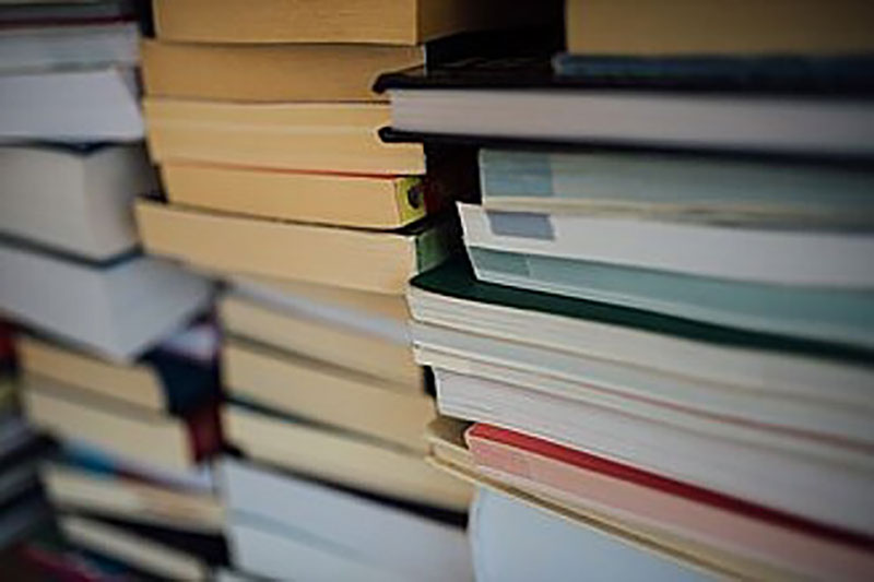 Ein Stapel Bücher in verschiedenen Größen und Farben, teilweise ineinander verschoben. Die Bücher sind dicht gestapelt und vermitteln den Eindruck von Wissen und Literatur.