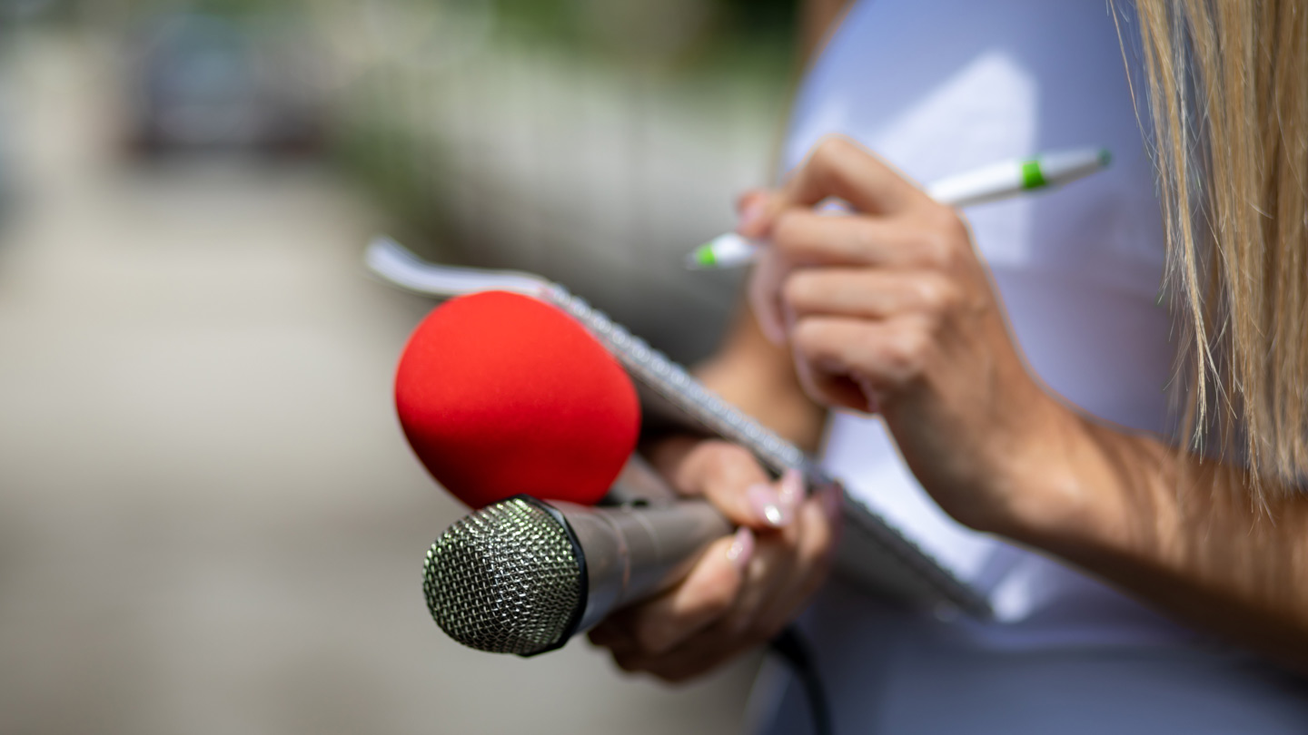 Eine Journalistin hält Mikrofone und einen Schreibblock