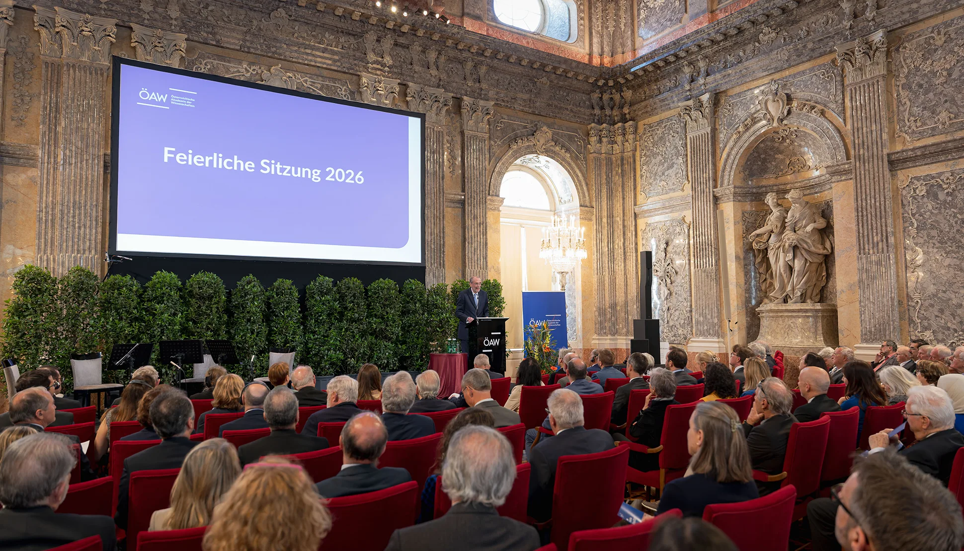 Foto aus dem voll besetzten Festsaal heraus auf die Bühne mit Heinz Faßmann neben einer großen Leinwand