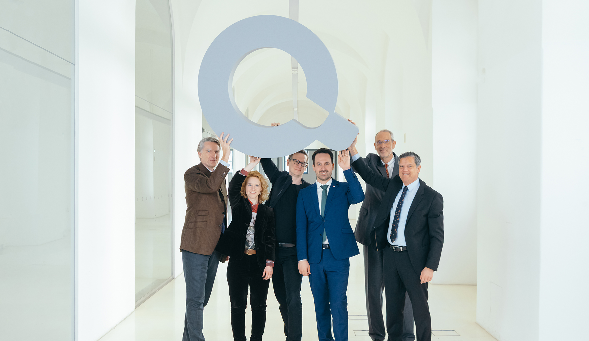 Mehrere Personen halten ein großes "Q" in die Luft