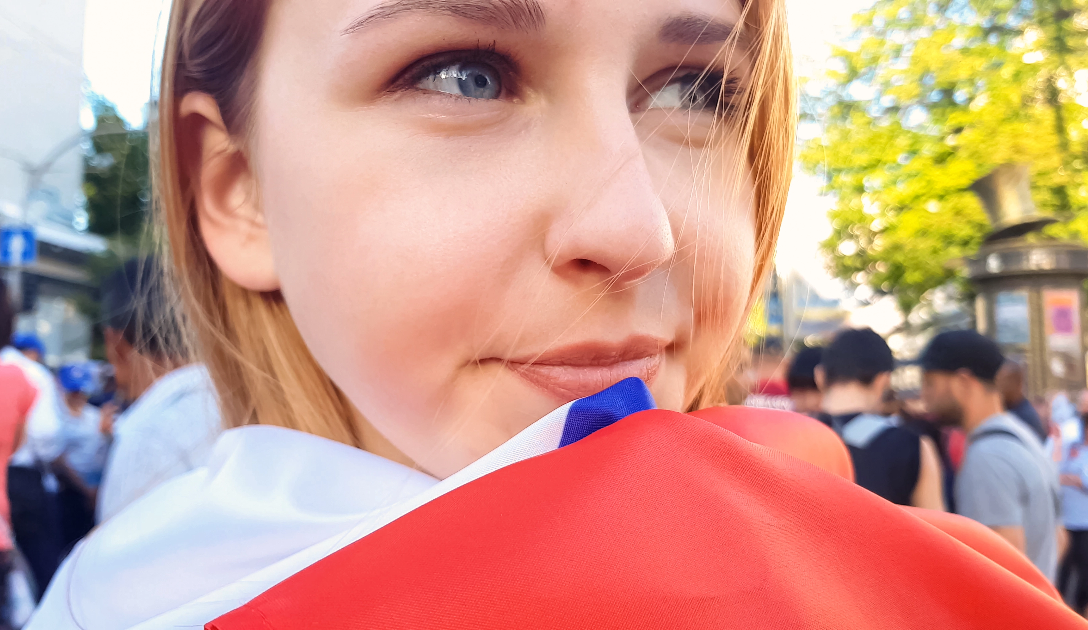 Eine junge Frau blickt hoffnungsvoll und hält sich eine serbische Flagge unter das Kinn