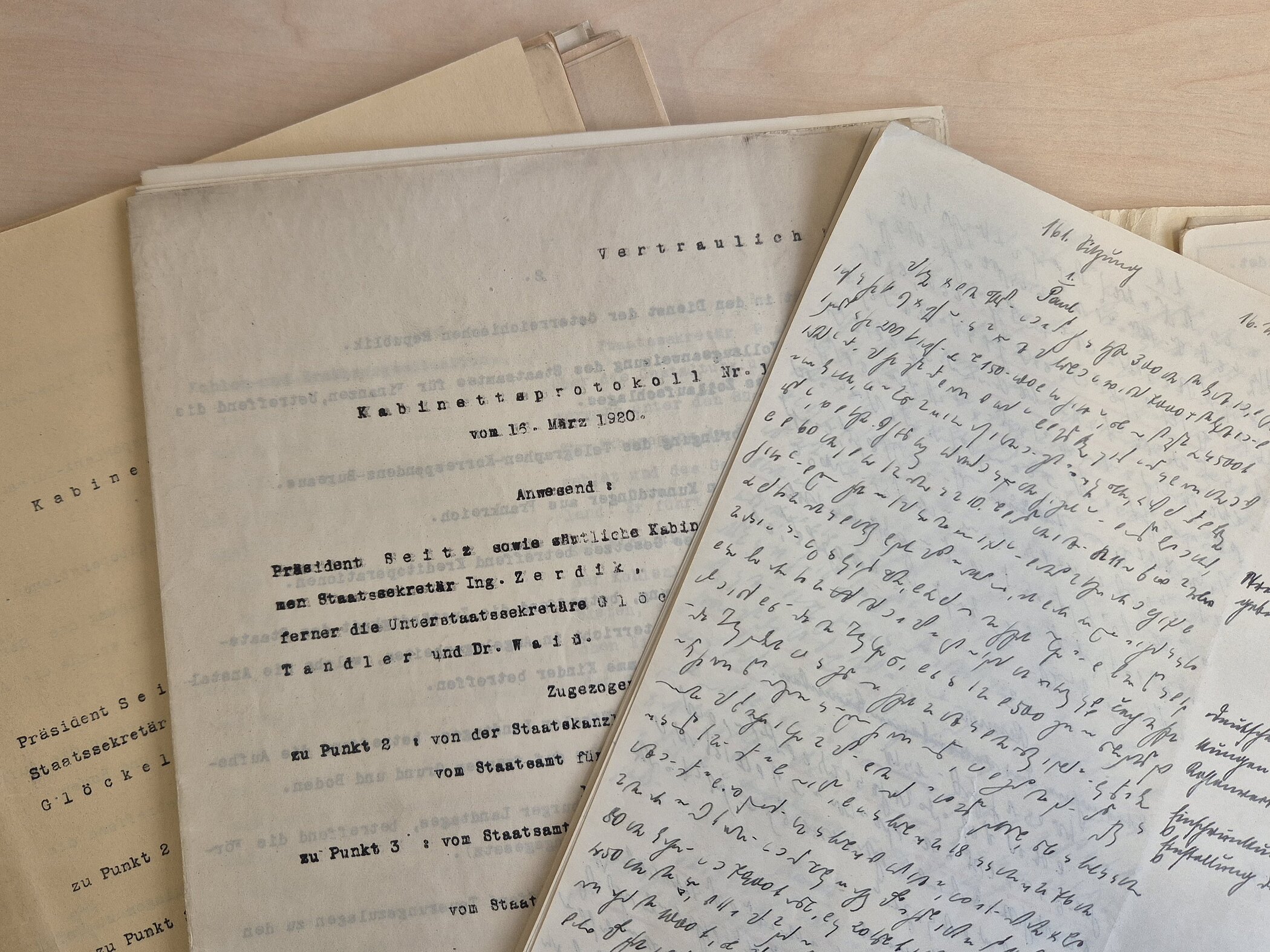 Photograph of some papers, overlapping. Two of them are written with typewriter, one is handwritten in shorthand and one is handwritten in Kurrentschrift.