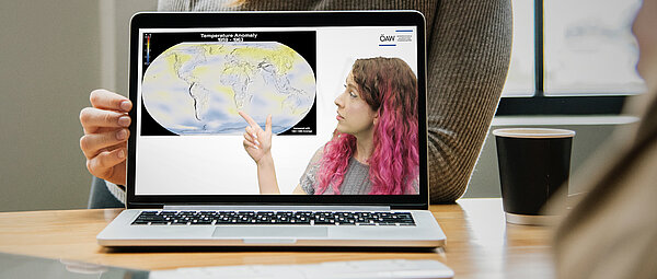Auf einem Tablet ist eine Dame zu sehen, die fragend auf eine Weltkarte mit eingefärbten Klimazonen zeigt
