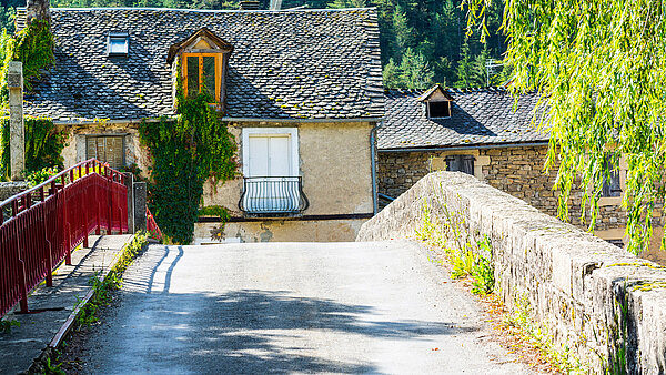 Foto einer alten steinernen Brücke, die in Richtung eines baufälligen Hauses führt