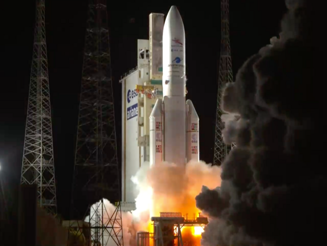 A large, white Ariane 5 rocket lifts off from the launch pad at night amid massive clouds of fire and smoke.