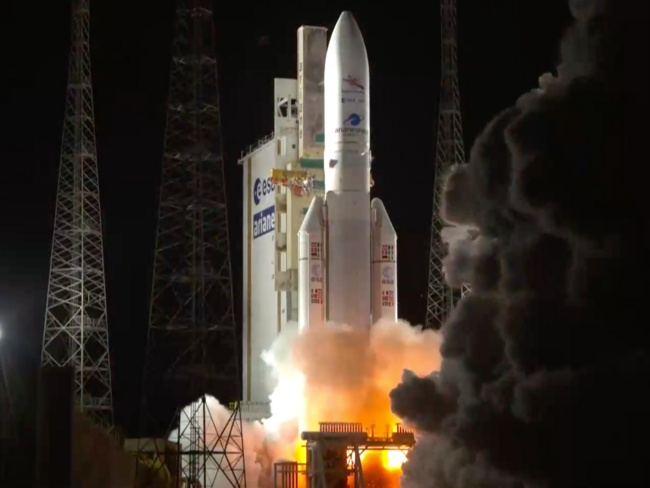 A large, white Ariane 5 rocket lifts off from the launch pad at night amid massive clouds of fire and smoke.