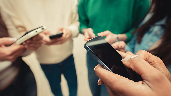 Eine Gruppe von Jugendlichen steht im Kreis und hält Smartphones in Händen