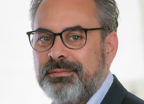 Porträt von Keywan Riahi mit Brille, grauem Bart und dunklem Sakko.