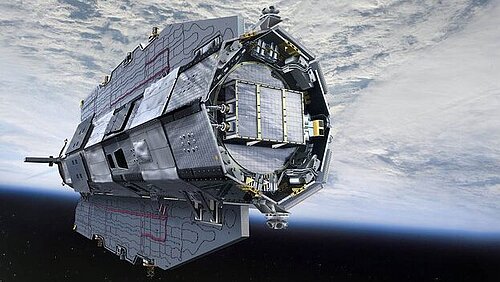 An elongated, metallic satellite with an aerodynamic shape hovers in near-Earth space. In the background, the Earth's surface is visible, largely covered by a thick, white cloud cover.