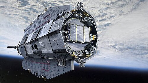 An elongated, metallic satellite with an aerodynamic shape hovers in near-Earth space. In the background, the Earth's surface is visible, largely covered by a thick, white cloud cover.
