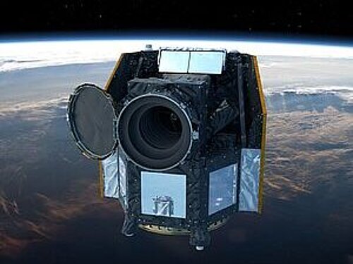 The digital illustration shows the CHEOPS hexagonal space telescope in Earth orbit with its round protective flap open in front of the lens. In the background, the globe is visible with bands of clouds and the thin blue strip of the atmosphere.