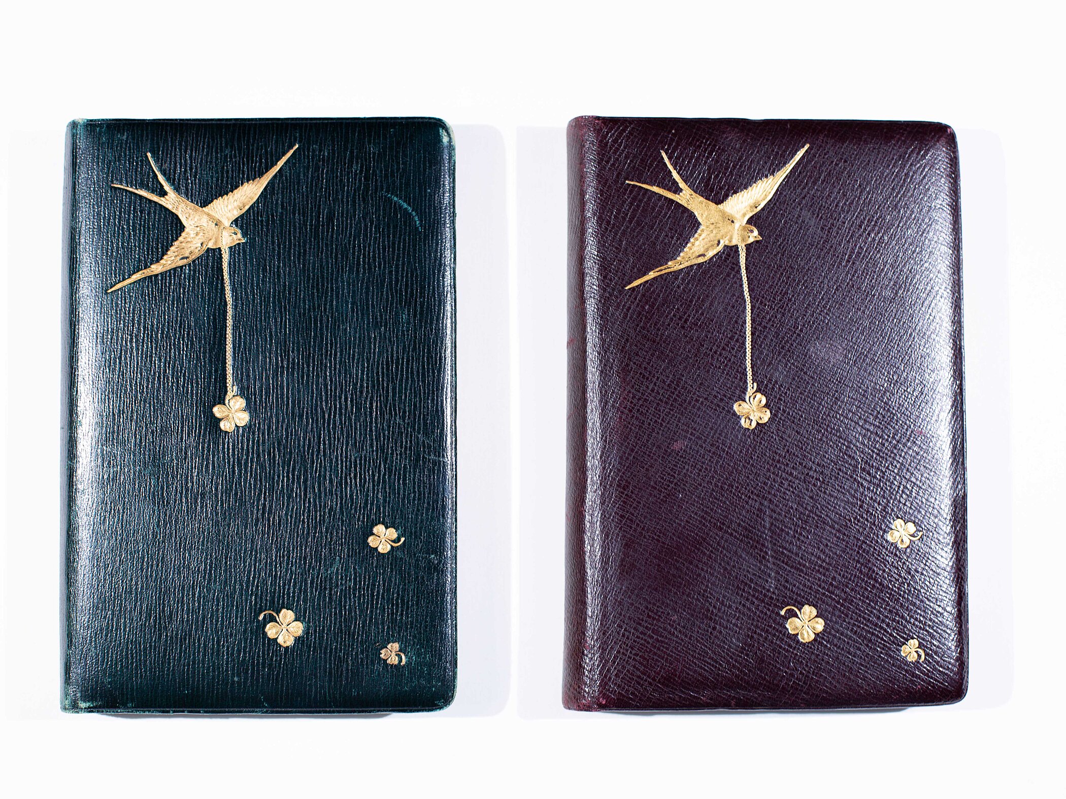 The covers of two leather-bound notebooks featuring the same golden illustration of a swallow and some flowers. The leather of the left one is black, the right one is a very dark red.