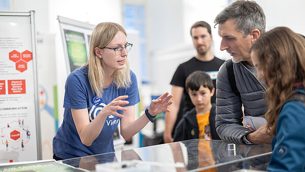 Eine ÖAW-Forscherin erklärt an einem Stand einer Gruppe von Menschen ein Ausstellungsstück