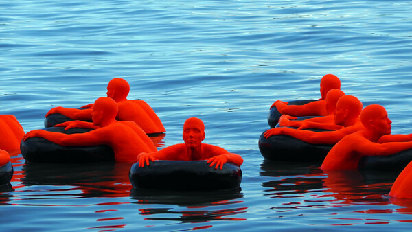 Eine Kunstaktion zeigt rot verkleidete Menschen, die auf Autoreifen im Meer schwimmen