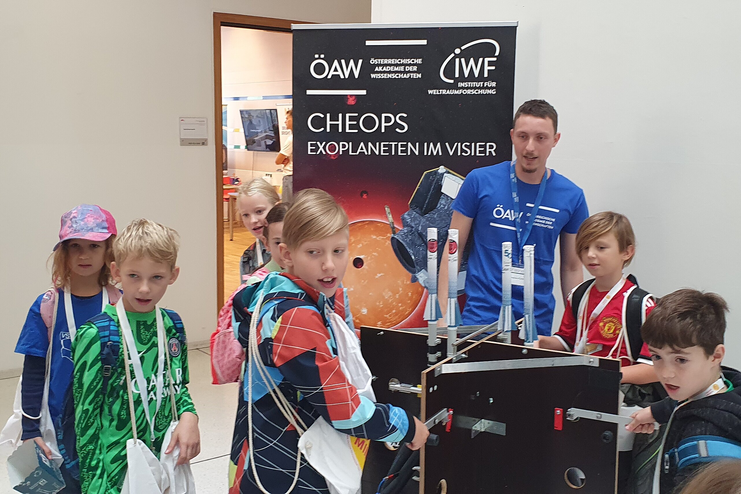 A group of kids looking at something behind the camera while they stand around a station about exoplanets.