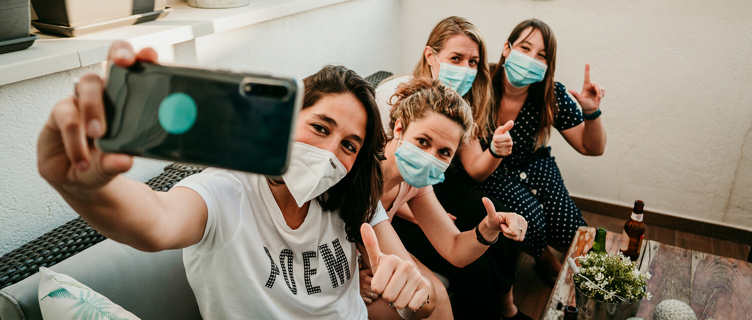 Eine Gruppe junger Frauen mit Masken sitzt zusammen und macht ein Foto von sich 