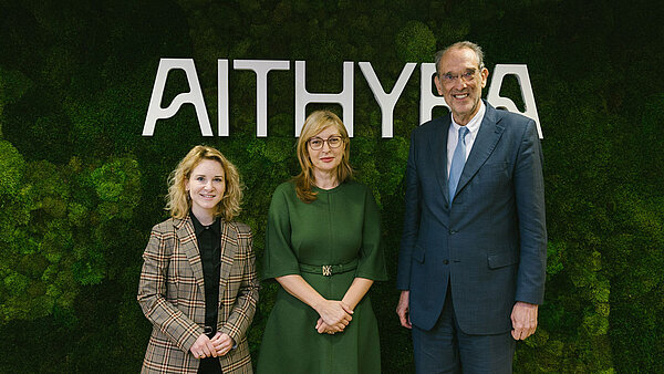 Drei Personen stehen vor einer Aithyra-Logowand.