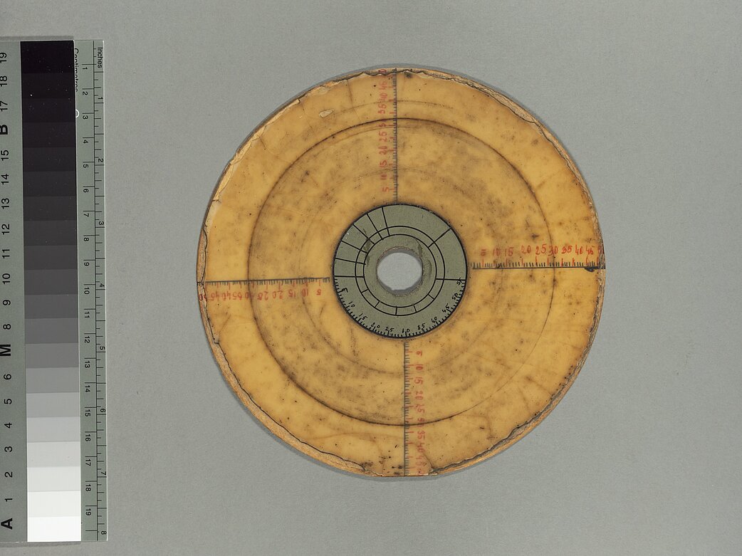 Abb. 5: Neben dem Graustufenkeil liegt eine gelbe 16,5 cm kleine Schallplatte mit grauem Etikett, vier Skalen im 90°-Winkel und sichtbaren Schmutzeinlagerungen.
