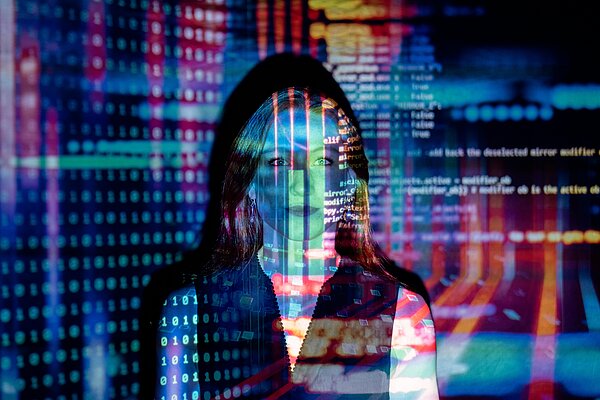 programming code projected onto the face of a woman and a screen behind her.