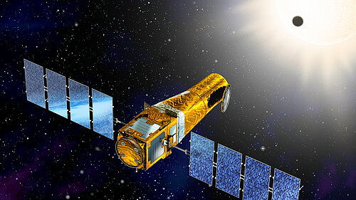 A golden, cylindrical satellite with two large, blue solar panel wings floats in deep space. In the background, a bright sun shines in the upper right corner, with a small, dark planet silhouetted against it as it transits across the sun.