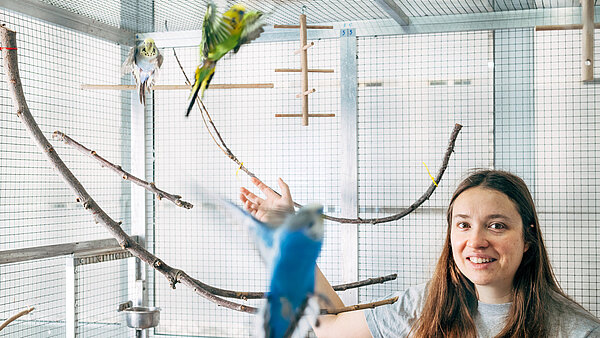 Eine Forscherin in einem Vogelgehege mit Papagei
