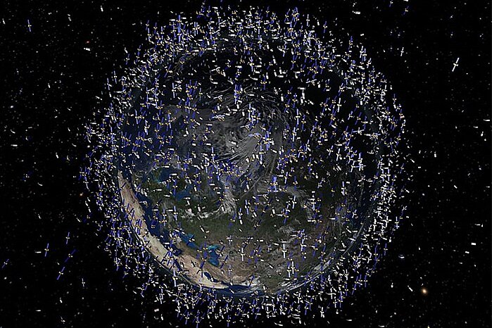 A computer graphic shows the planet Earth, surrounded in the pitch-black expanse of space by a dense, circular swarm of countless small, white satellite models.