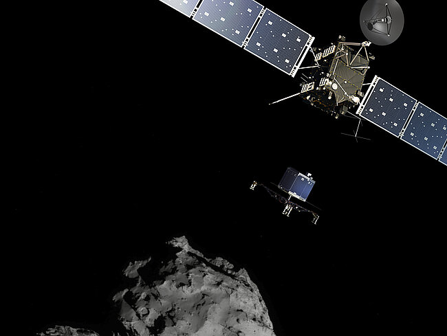 The Rosetta space probe, with its long solar panels, hovers in space above an irregularly shaped, gray comet.