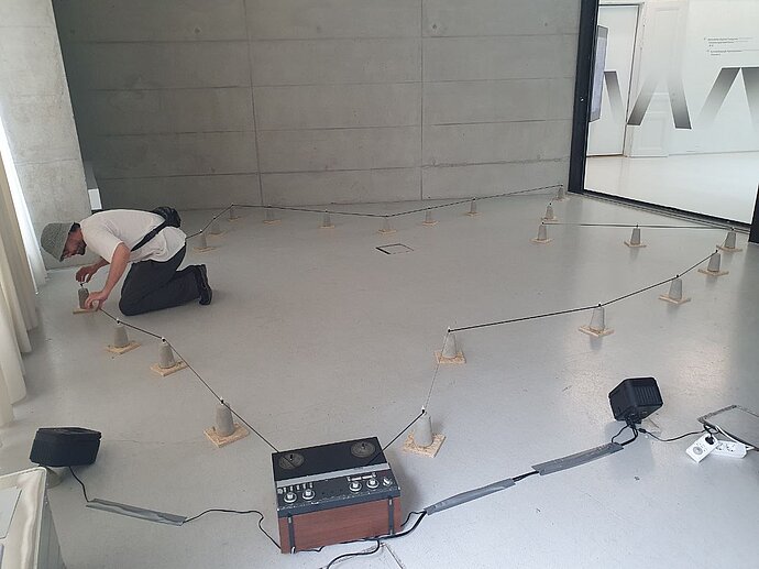 Installation: Ein Tonband wird über ein Loop, das quer durch den Raum läuft, mit einer Tonbandmaschine abgespielt.
