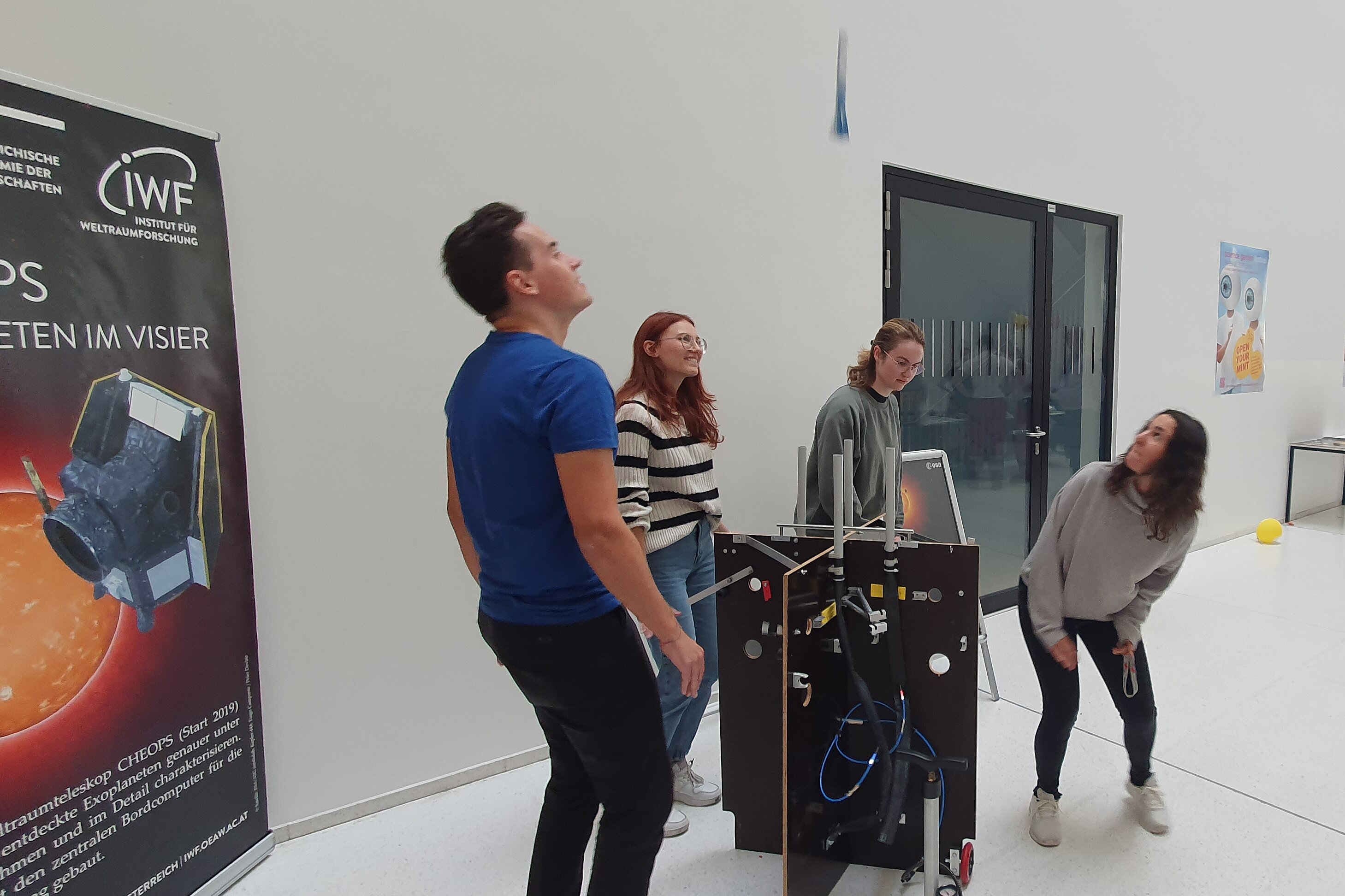 The picture shows a group of people in the middle of an experiment, where a miniature rocket is launched from a technical structure.