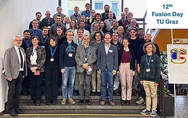 Gruppenfoto von mehreren Personen auf einer Treppe, rechts ein Schild mit dem Schriftzug '12th Fusion Day TU Graz'.