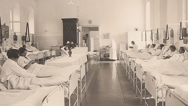 Historische Aufnahme eines Krankensaals mit zahlreichen Betten und Patient:innen