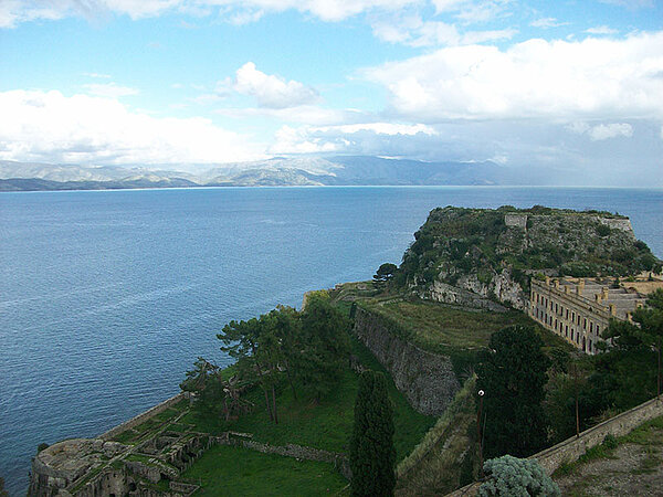 Blick über das Meer und die Küste von Korfu. Im Vordergrund liegt die Alte Festung von Korfu-Stadt mit ihren historischen Befestigungsanlagen; im Hintergrund ist die albanische Küste zu sehen.