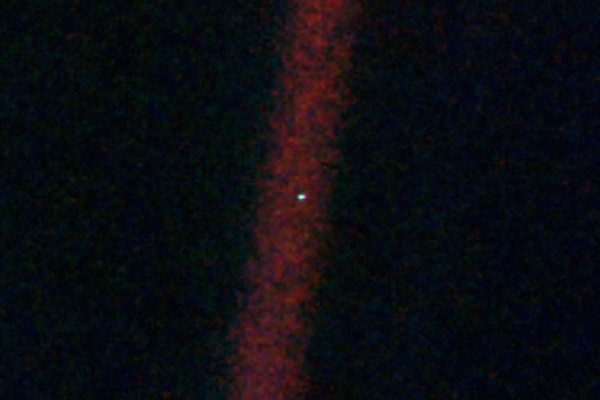 Astronomische Aufnahme der Erde („Pale Blue Dot“) als winziger, heller Punkt inmitten eines vertikal verlaufenden, rötlichen Lichtstreifens im dunklen Weltall.
