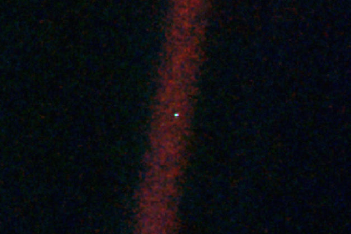 Astronomische Aufnahme der Erde („Pale Blue Dot“) als winziger, heller Punkt inmitten eines vertikal verlaufenden, rötlichen Lichtstreifens im dunklen Weltall.